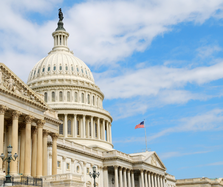 The U.S. Capitol building in Washington, D.C., featuring its white dome, columns, and an American flag, set against a partly cloudy blue sky.