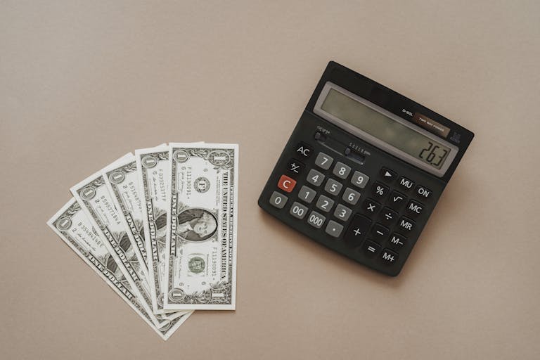 A calculator displaying '26.3' beside four one-dollar bills on a beige background.