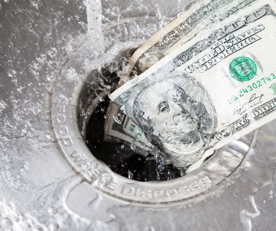 A stack of one hundred dollar bills being washed down a kitchen sink drain with water running, symbolizing a business losing profits